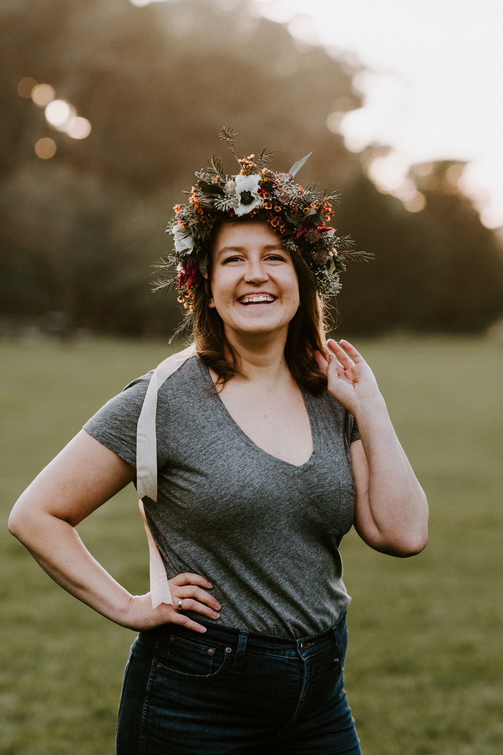 Photo of Lara standing in a field of grass, wearing a flower crown and smiling at the camera