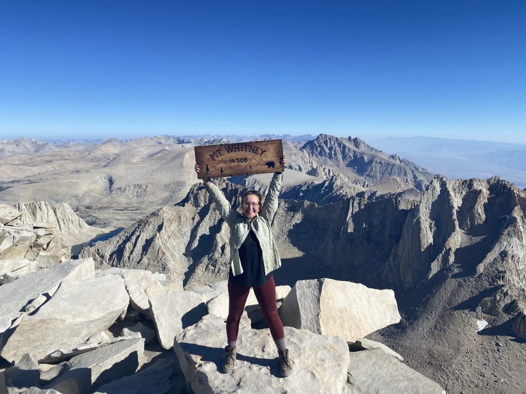 Lara standing on top of Mount Whitney next to the summit sign