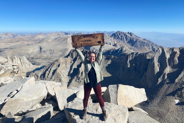 Lara standing on top of Mount Whitney next to the summit sign